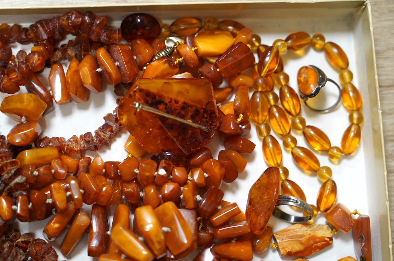 Five assorted single strand amber necklaces, including jagged pebble and unpolished, longest 176cm, together with two mounted amber rings, a pair of ear clips and a brooch, gross weight 357 grams. Condition - poor to fai